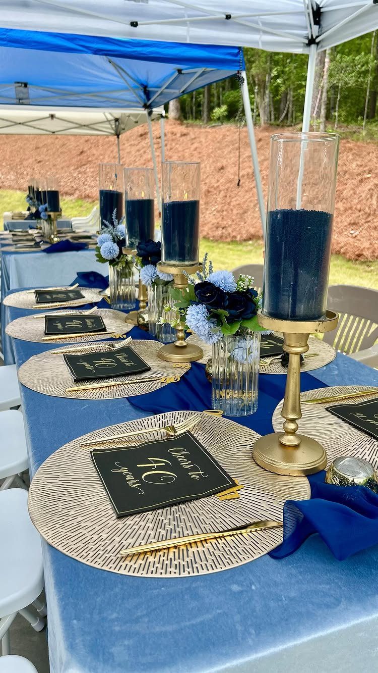 Elegant outdoor table setting with blue linens, gold chargers, and tall blue candles.