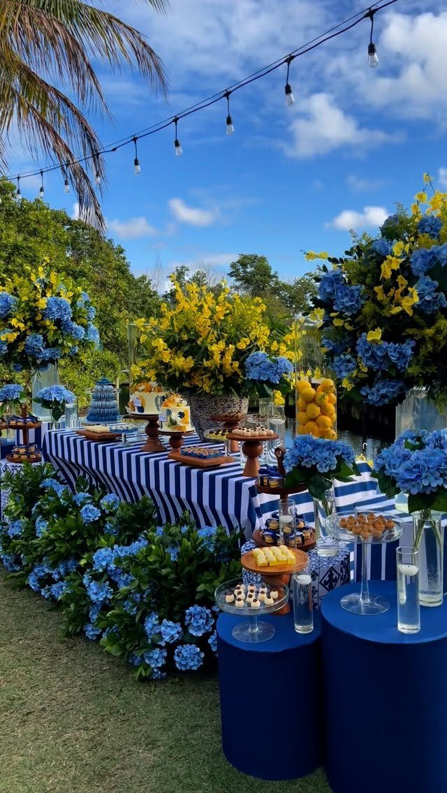 Outdoor party table with blue and yellow floral arrangements and overhead string lights.
