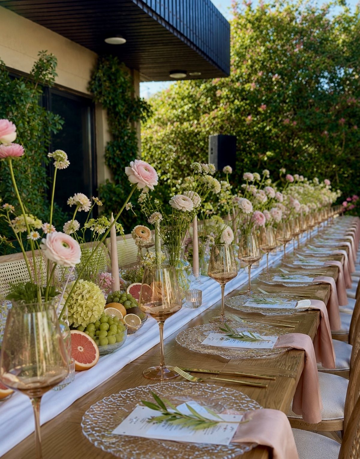 Long wooden dining table with pink floral arrangements, gold cutlery, and elegant place settings.