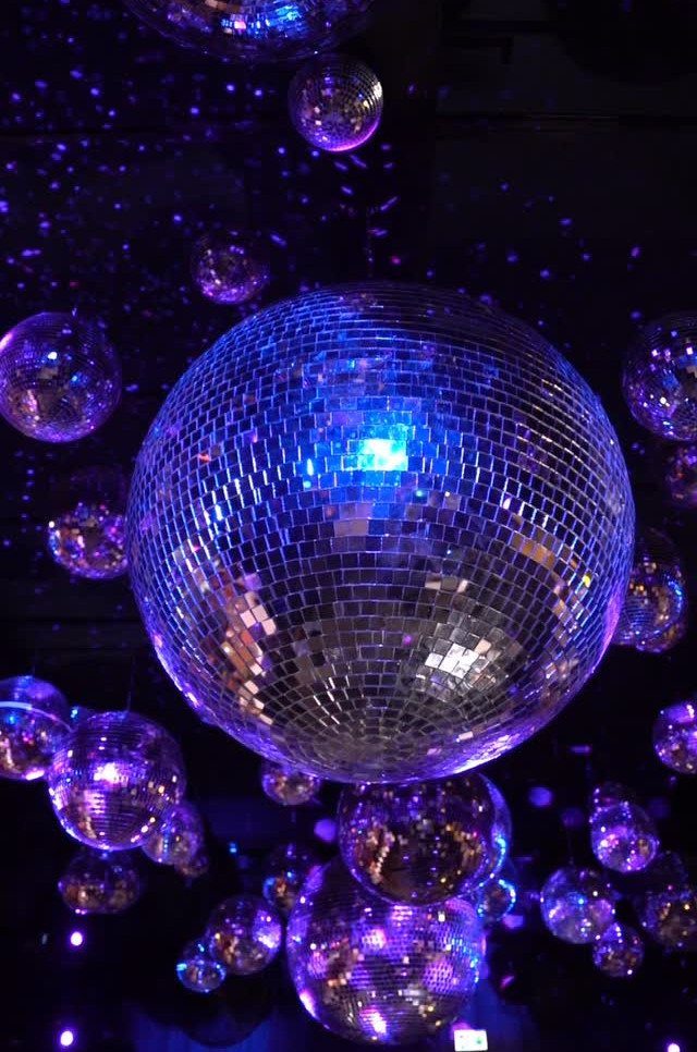 Mirrored disco balls of different sizes hanging in a dark room with blue lighting.