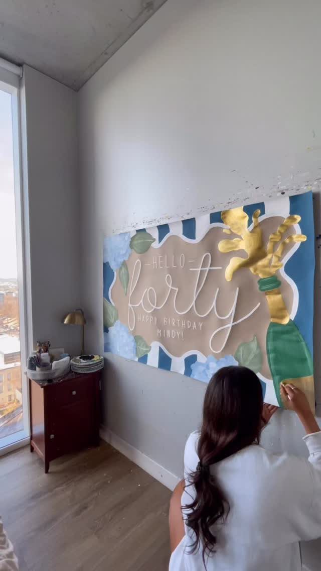 Woman painting a handmade birthday banner with champagne and the word forty.