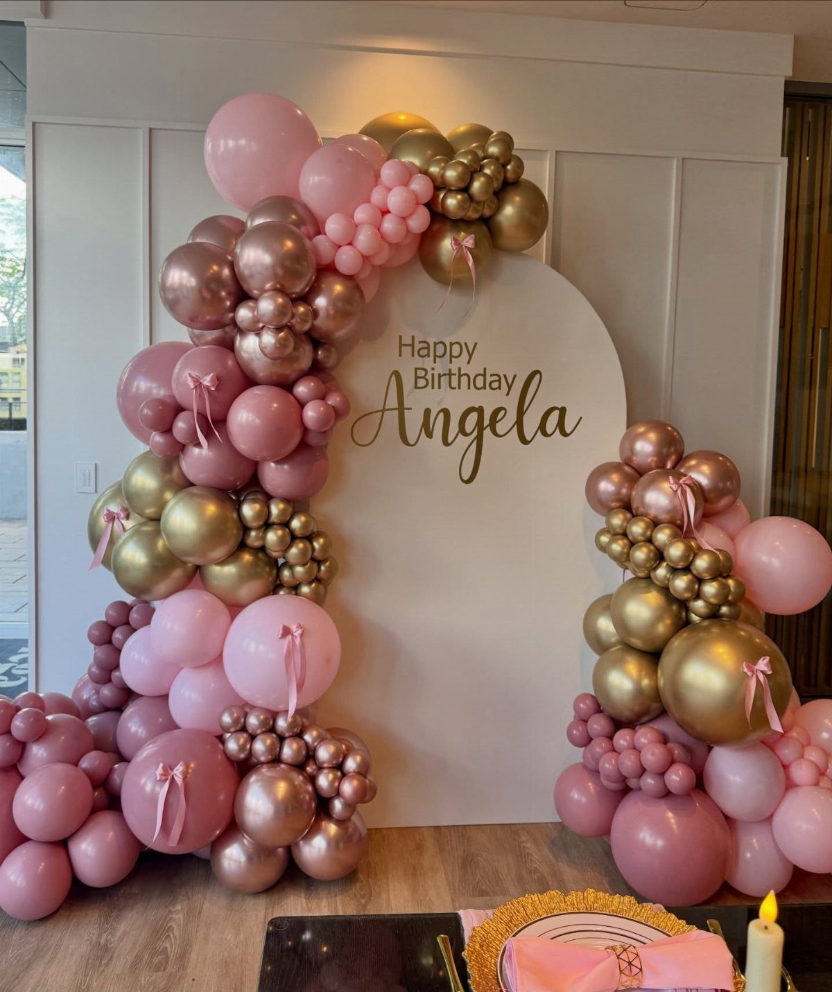 Rose gold and pink balloon garland surrounding a white birthday backdrop for Angela.