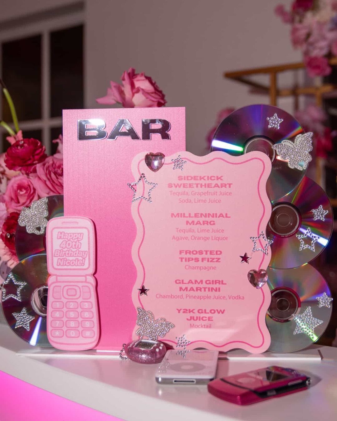 Pink bar setup with a cocktail menu, CDs, and Y2K themed accessories.