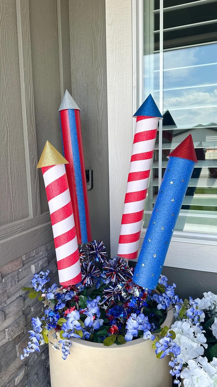 Oversized red, white, and blue firecracker pool noodle decorations in a flower planter.