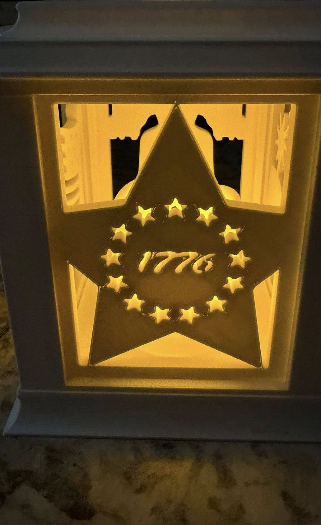 White lantern with a star cutout and 1776 glowing with warm yellow light.