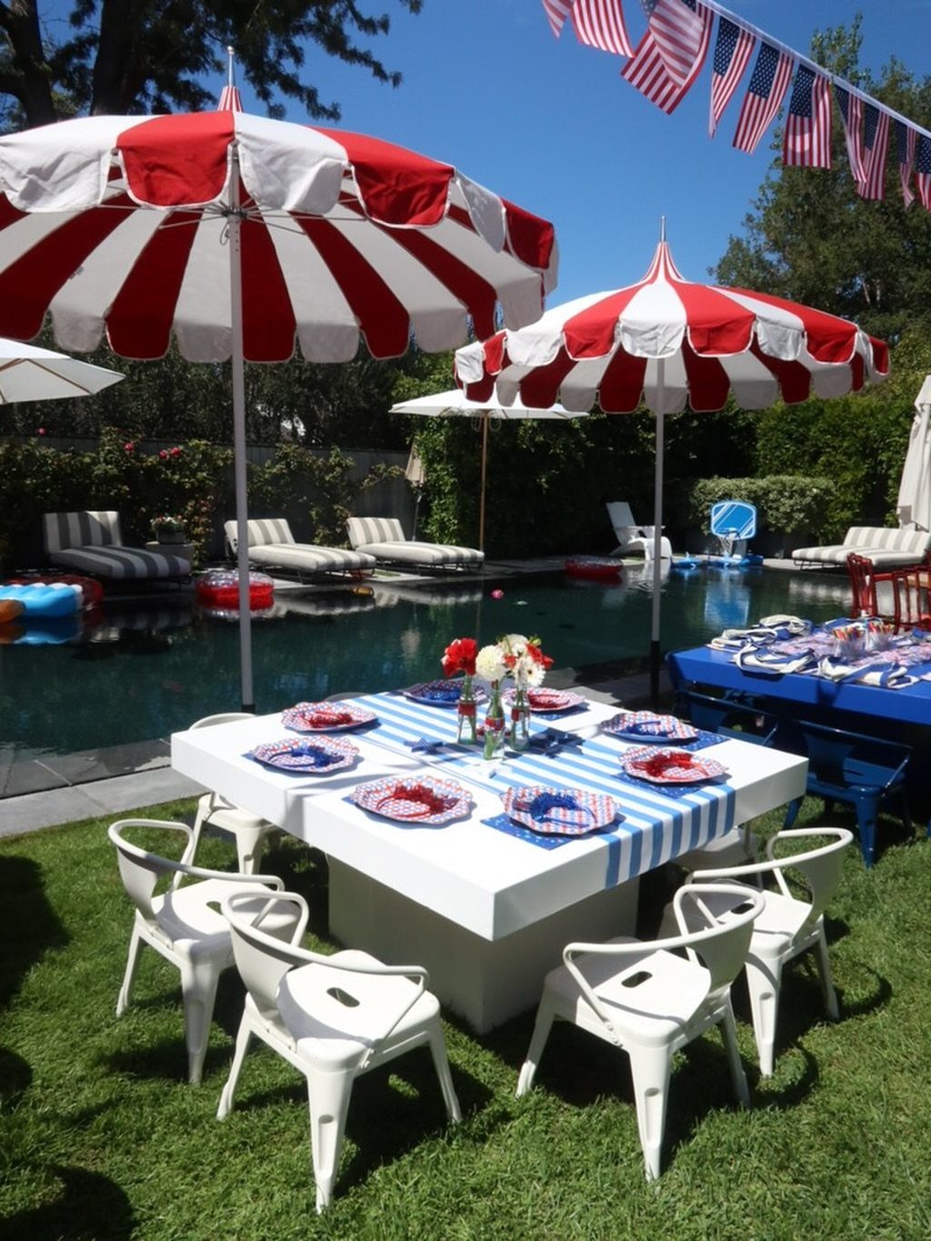 Red and white striped umbrellas shading a patriotic poolside dining table and chairs.
