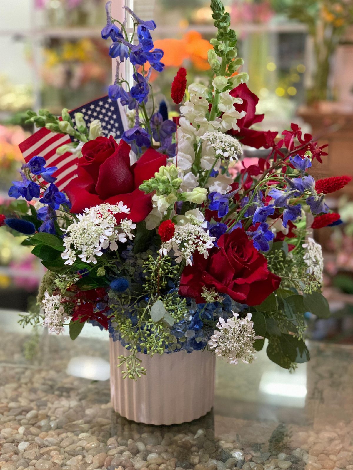 Red, white, and blue floral arrangement with a small American flag in a pot.