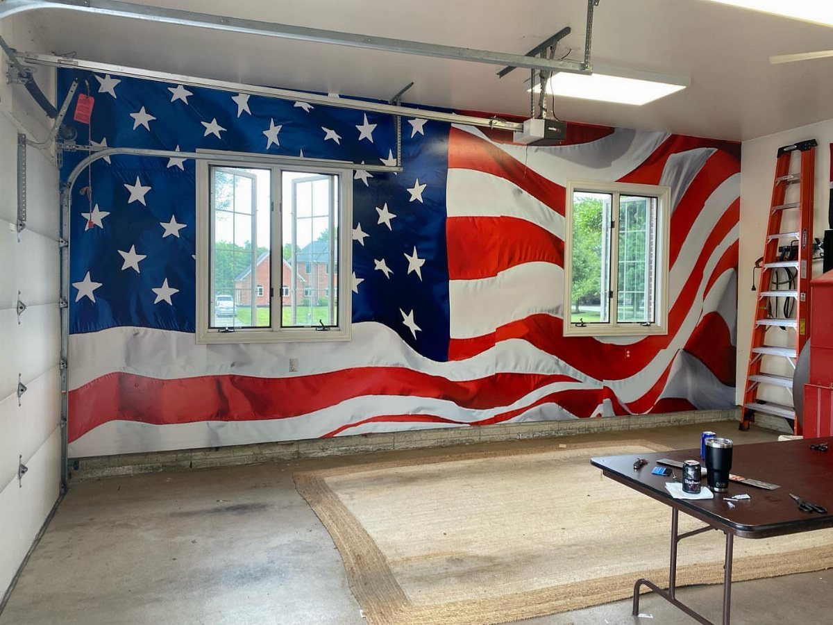 Large American flag draped across a garage wall between two white windows.