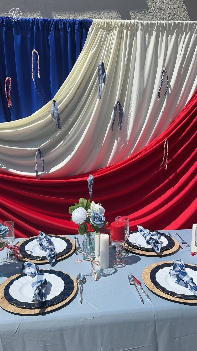 Patriotic table setting with blue cloth, white plates, and red white blue backdrop.