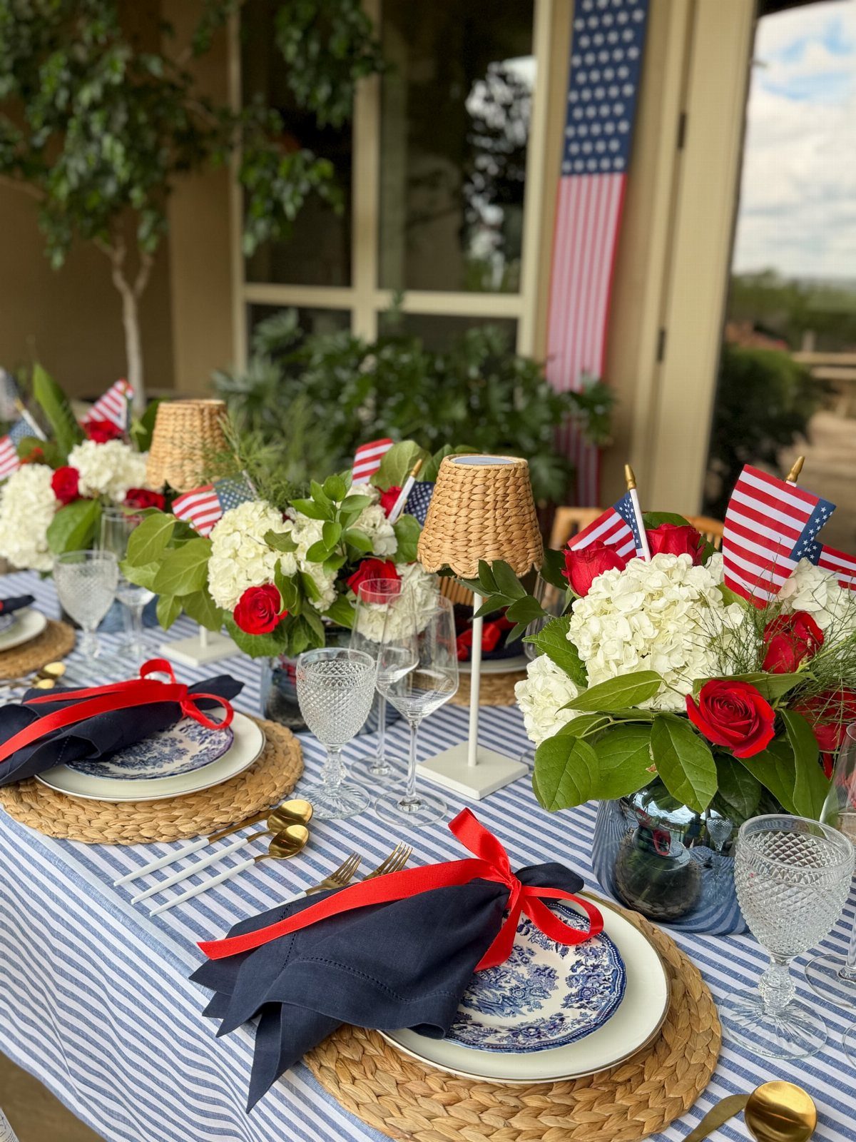 Patriotic table setting with striped tablecloth, red and white flowers, and American flags.