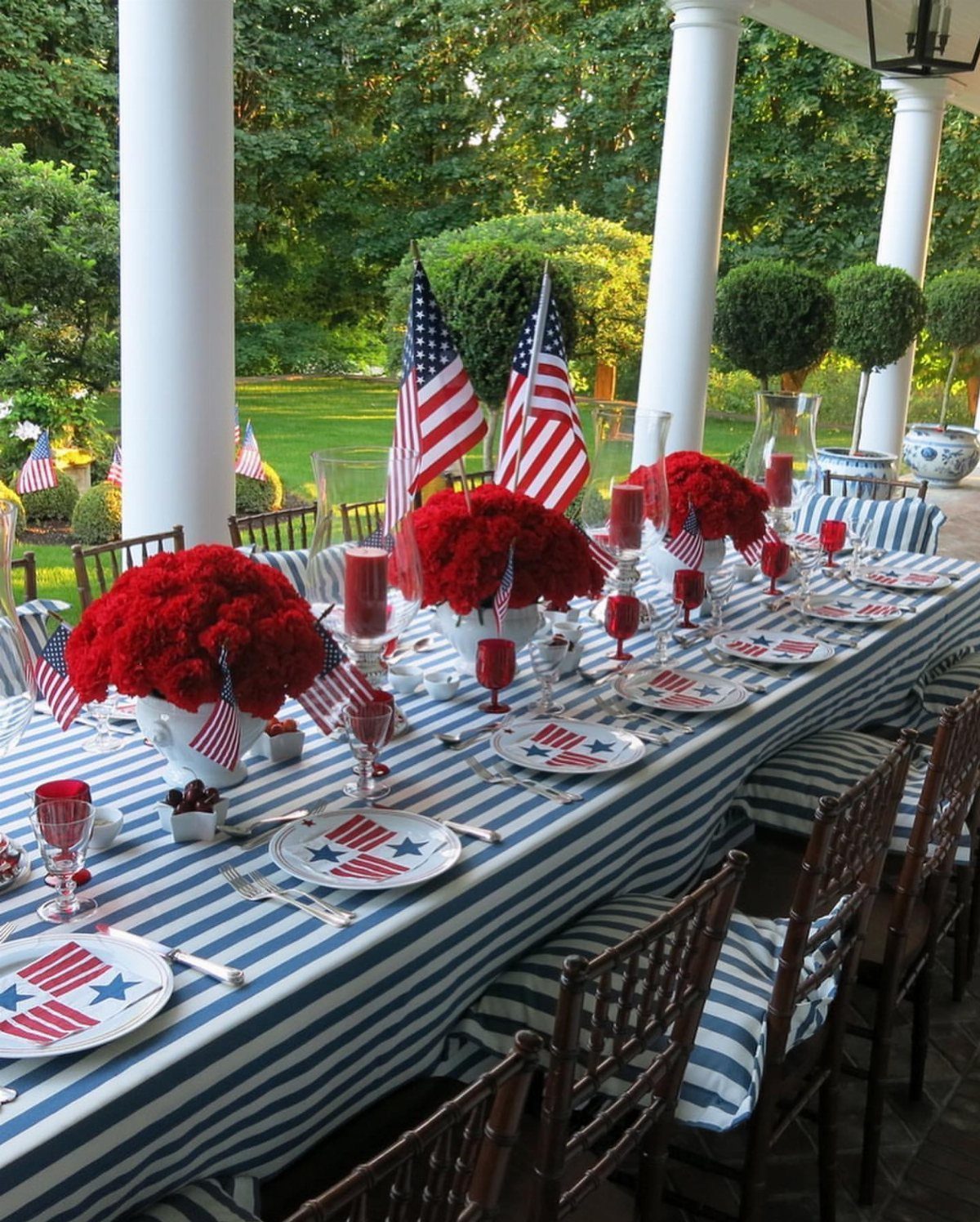 Patriotic 4th of July tablescape with red flowers, American flags, and striped linens.