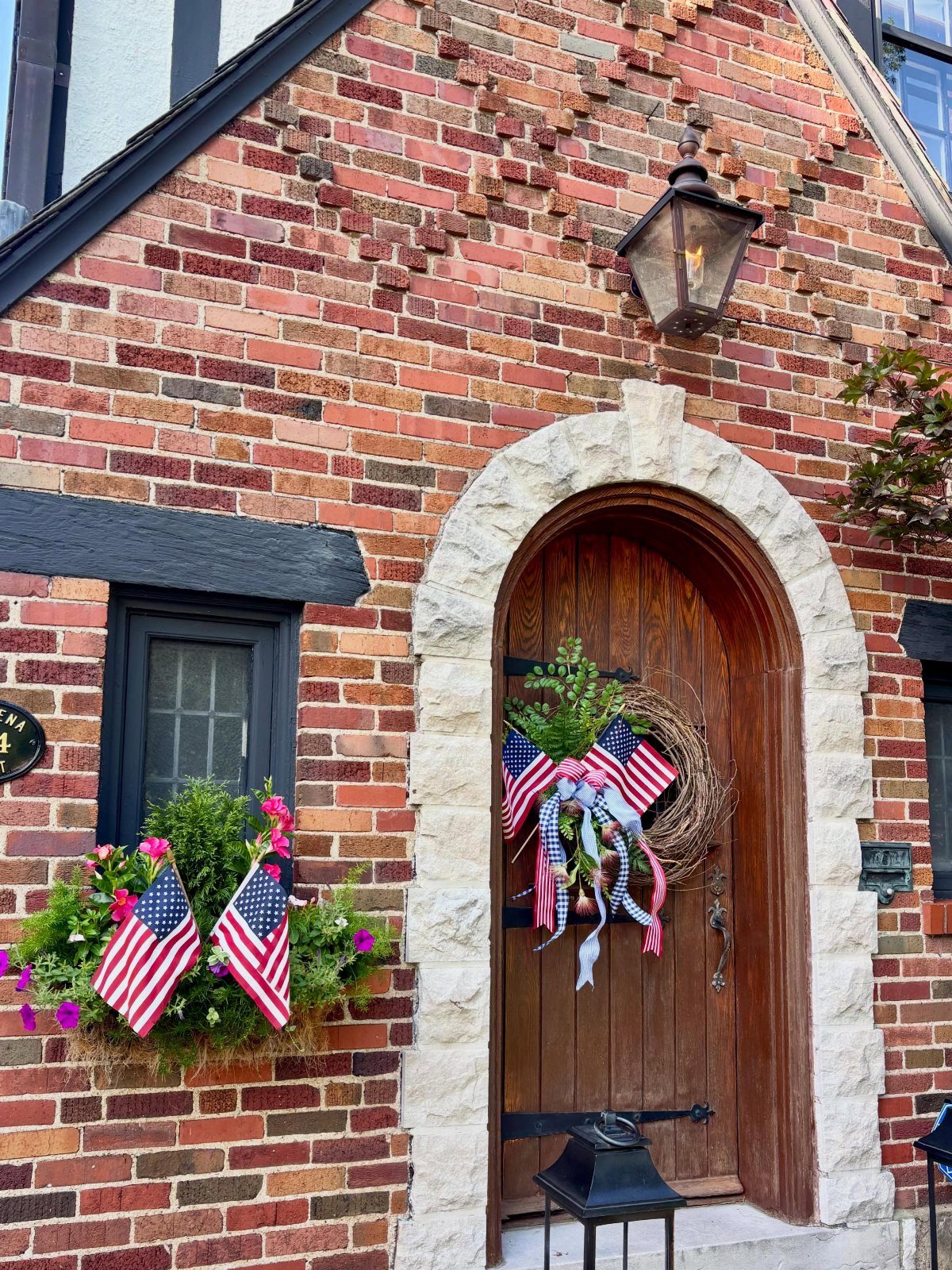 American flag decorated wreath hanging on a wooden arched door of a brick house