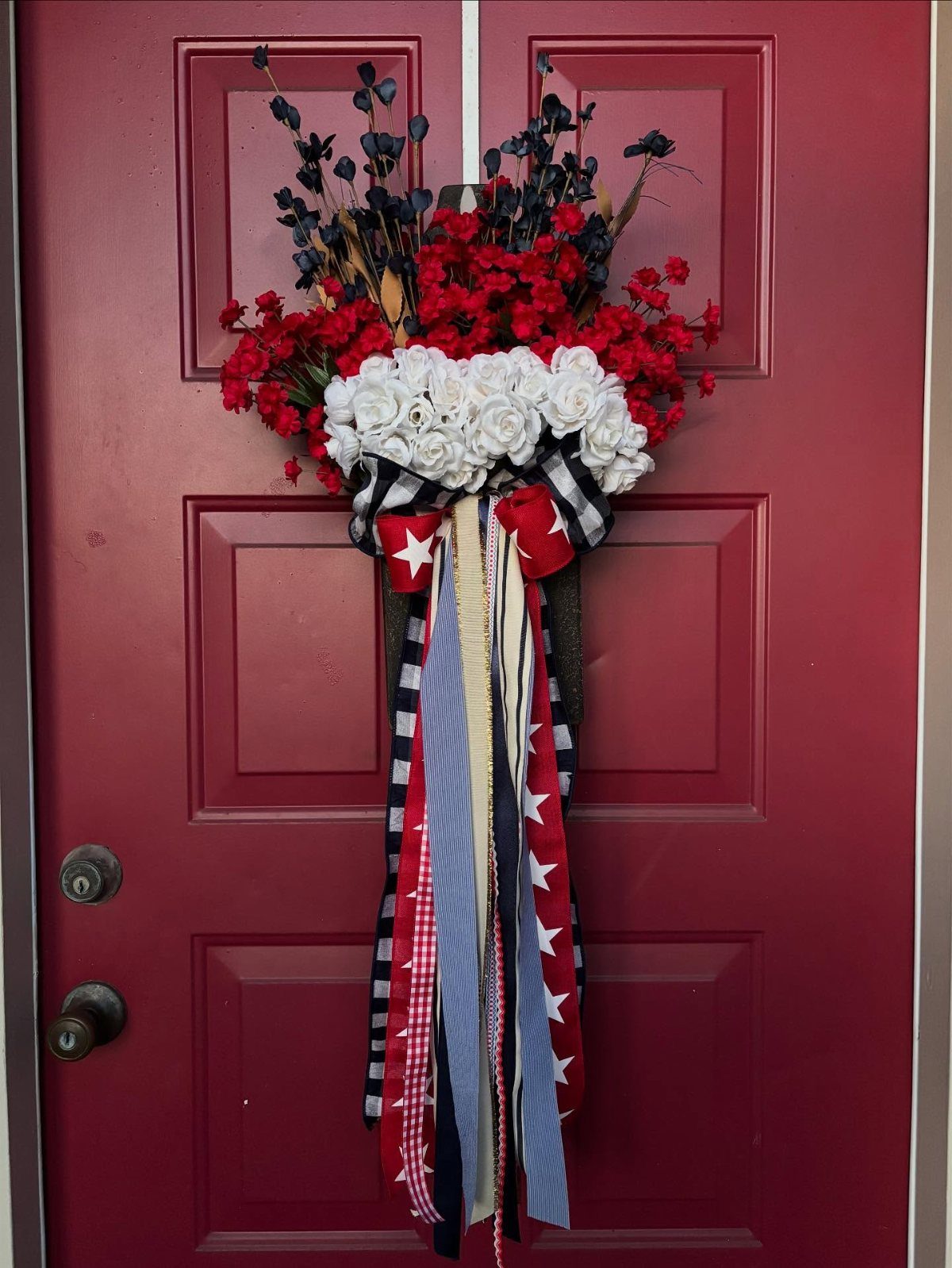 Patriotic floral wreath with red and white flowers and ribbons on red door