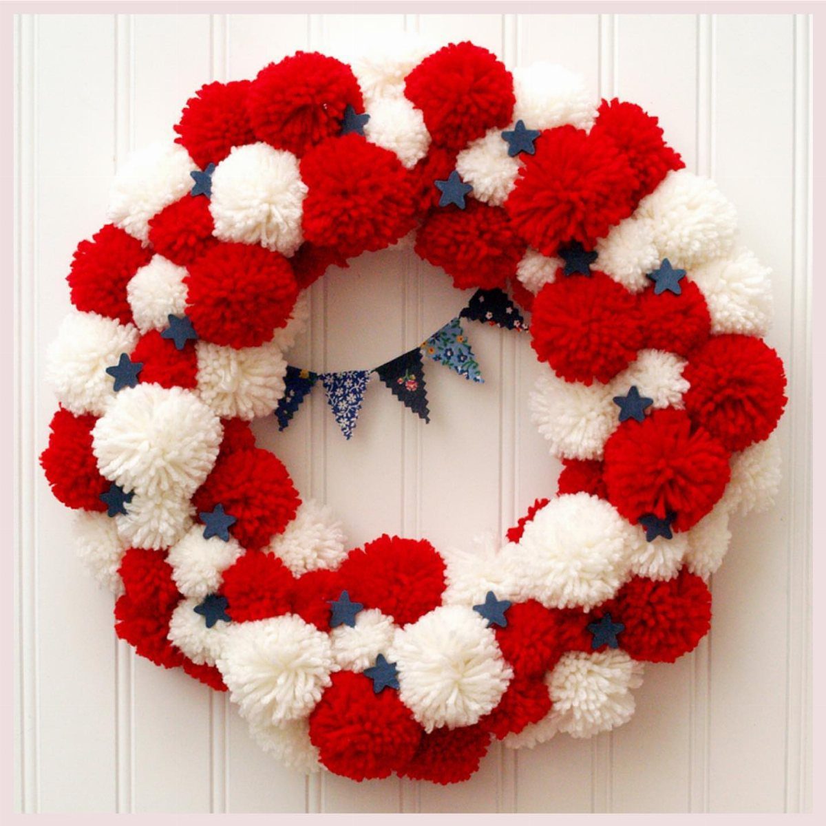 Red, white, and blue pom-pom wreath with stars on a white paneled wall