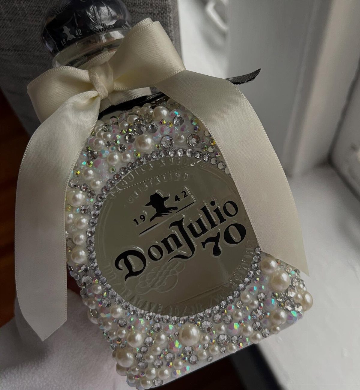 Don Julio tequila bottle embellished with white pearls, rhinestones, and a satin bow.