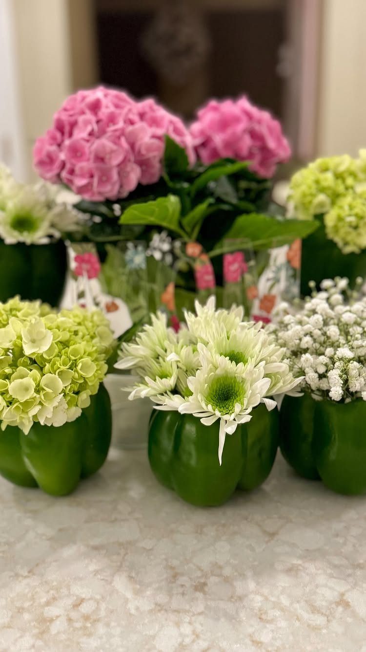 Green bell peppers used as vases for white and yellow flowers on a counter.