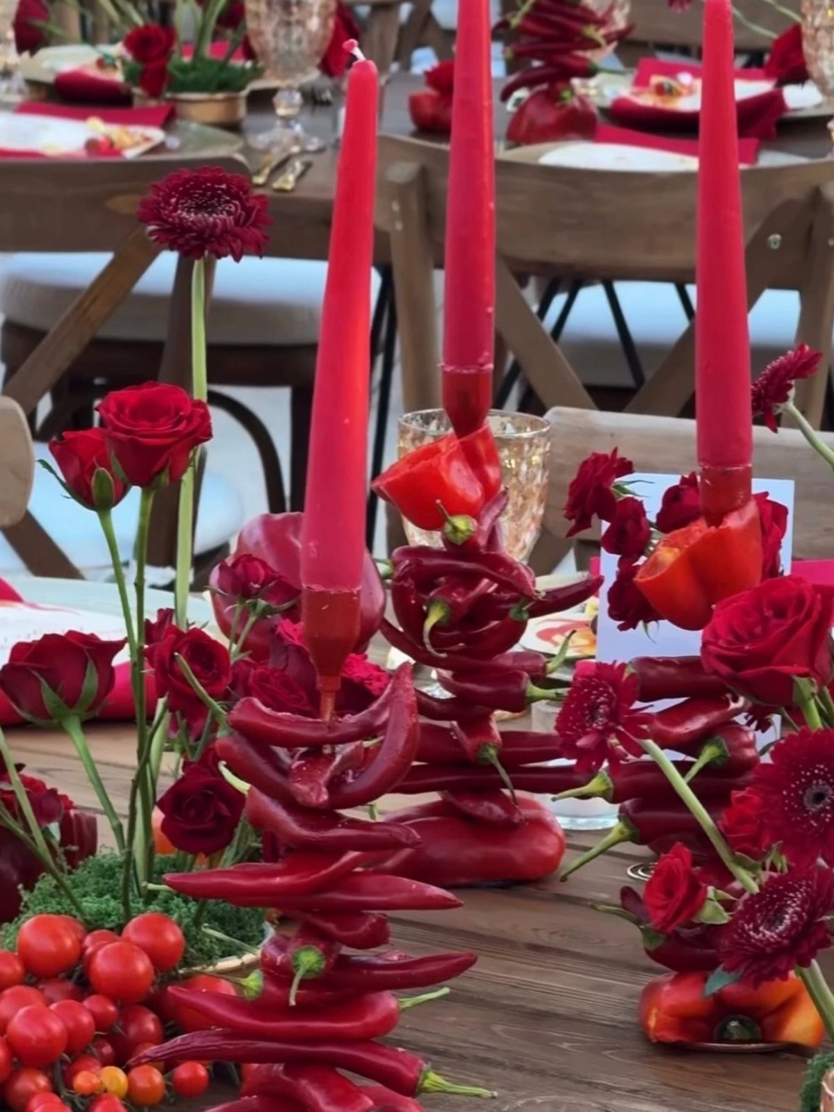 Red taper candles supported by stacked red chili peppers and red roses.