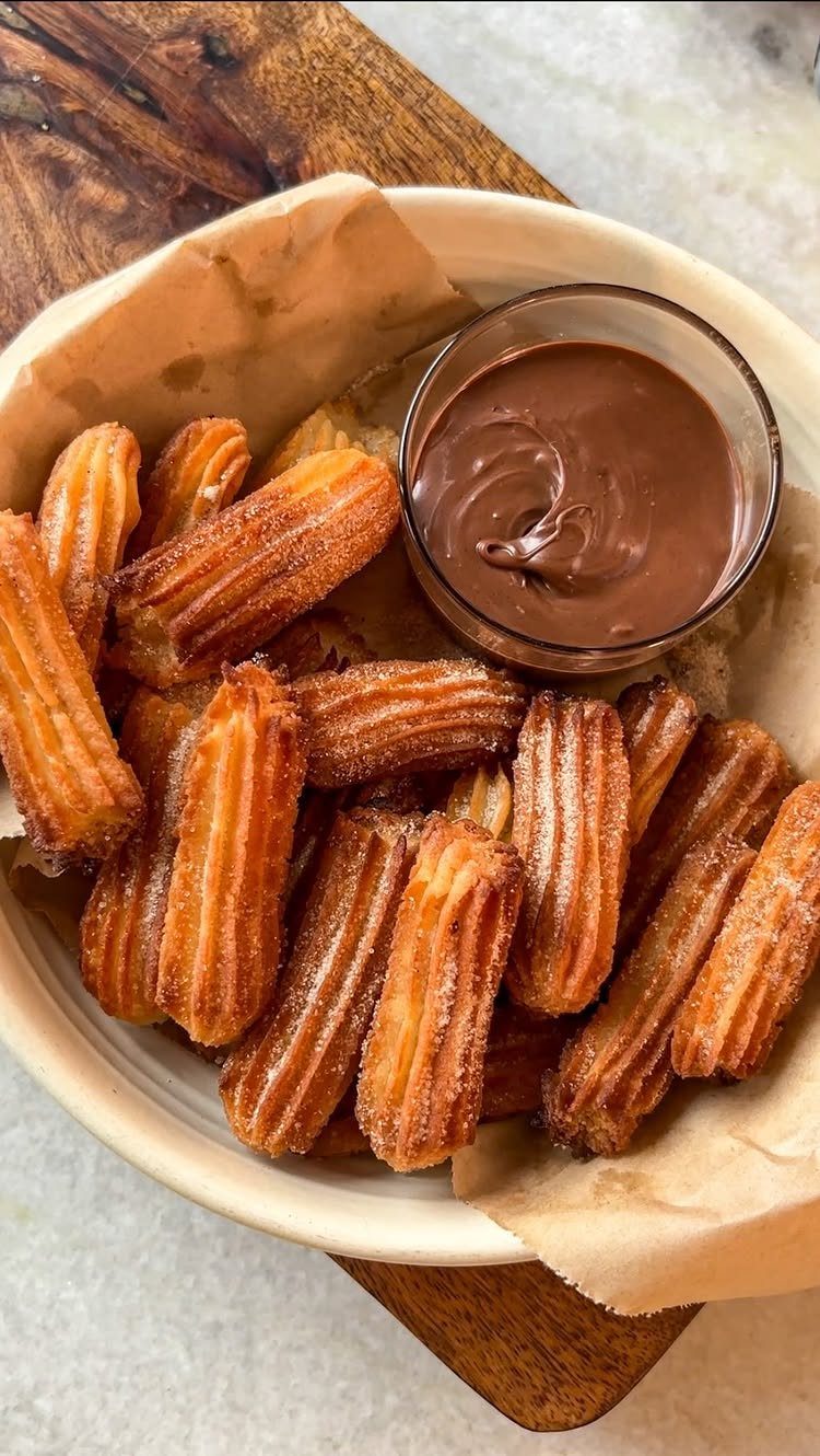 Cinnamon sugar churros in a white bowl with a side of chocolate sauce.