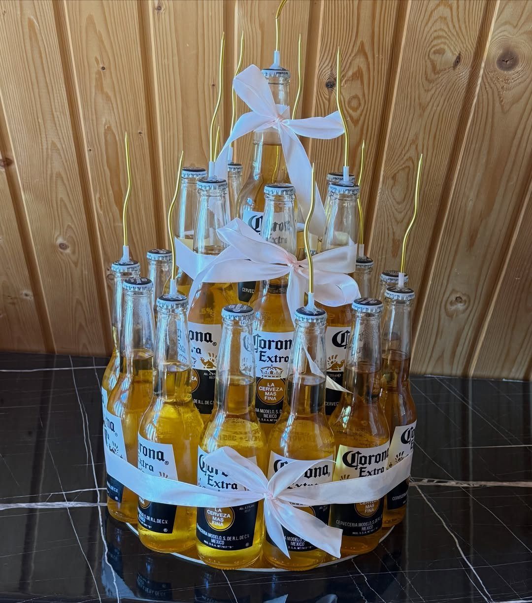 Corona beer bottles arranged in a circle with pink ribbons and gold candles.