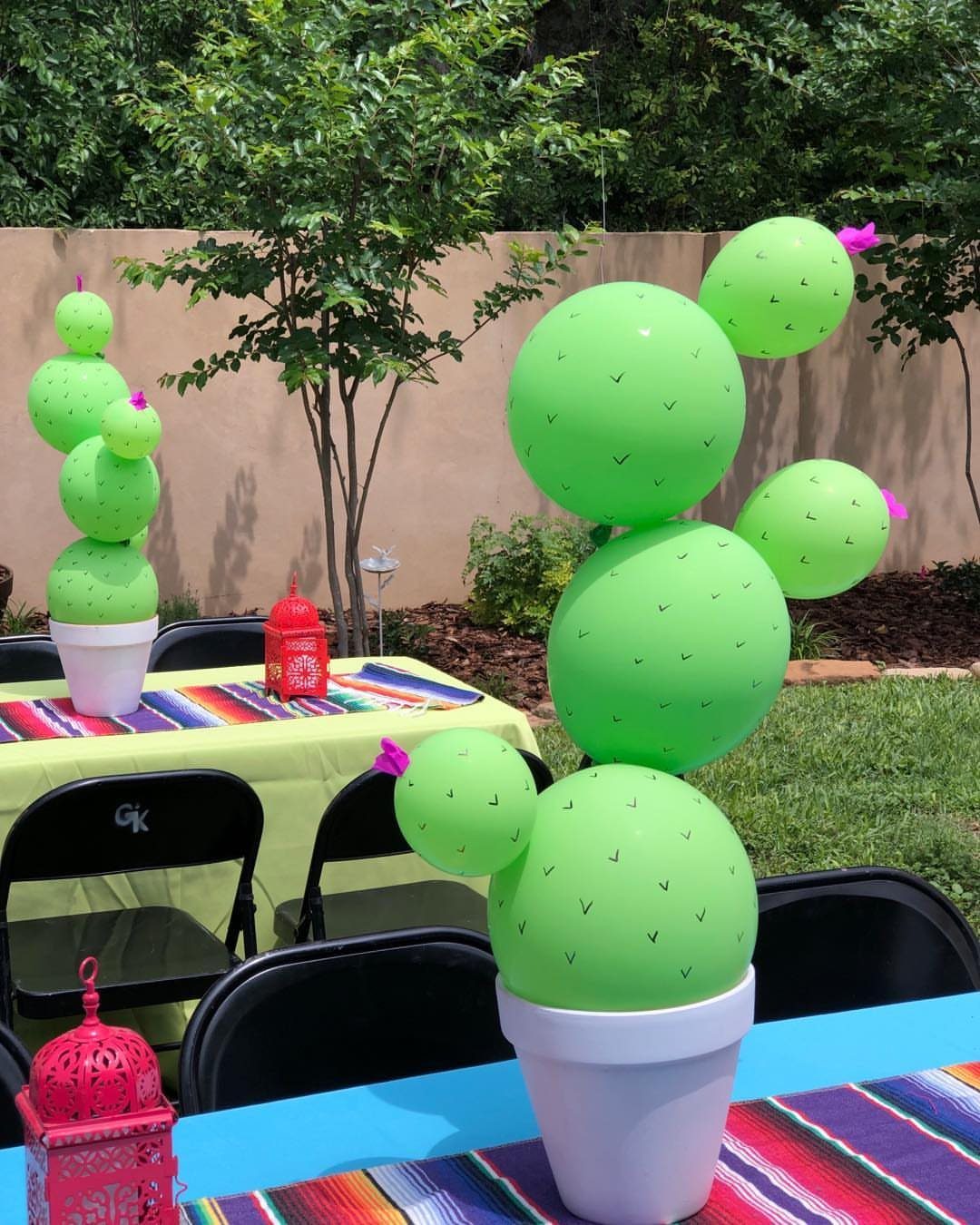Green balloon cacti in white pots on tables with colorful serape runners outdoors.