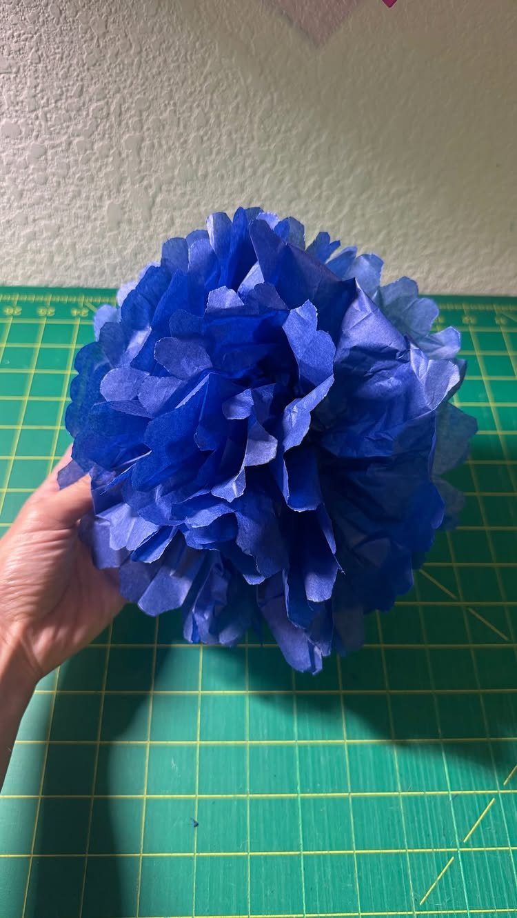 Large blue tissue paper flower held by a hand over a green mat.