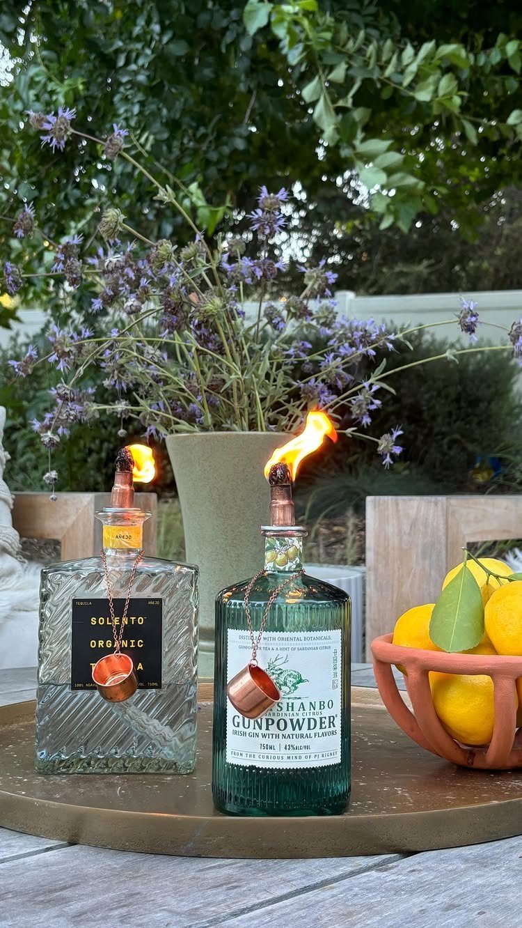 Repurposed liquor bottle tiki torches with flames on a gold tray with lemons.