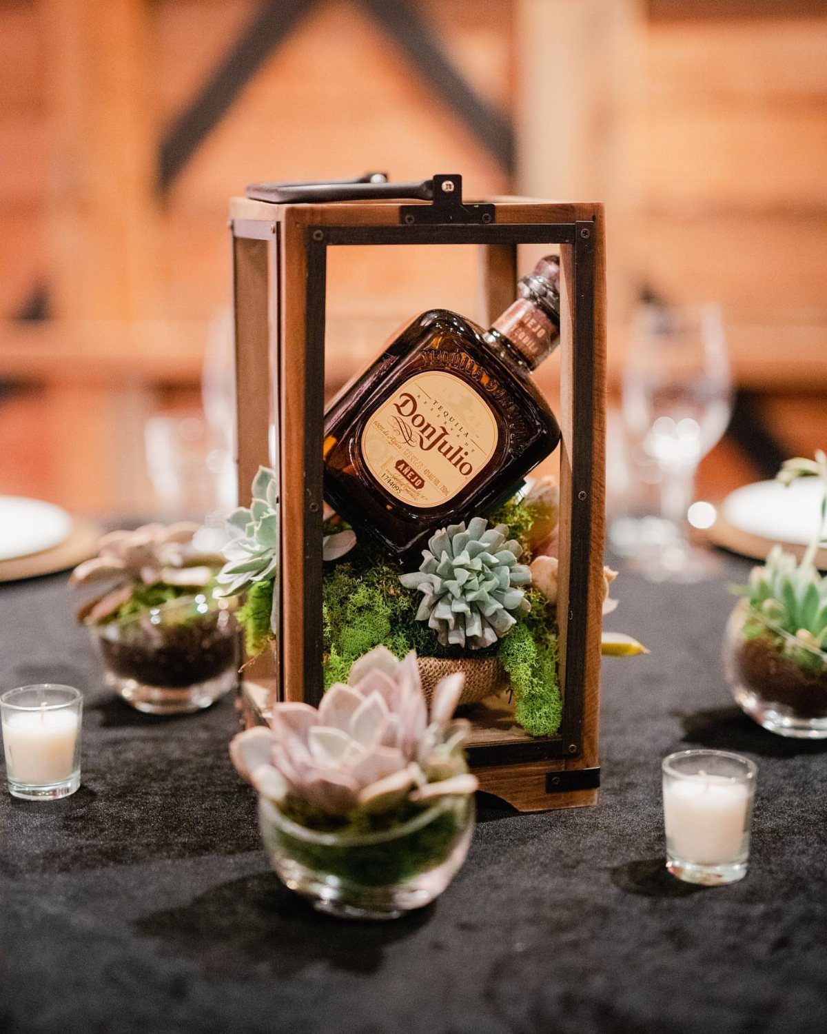 Tequila bottle inside a wooden lantern with succulents and moss on a table