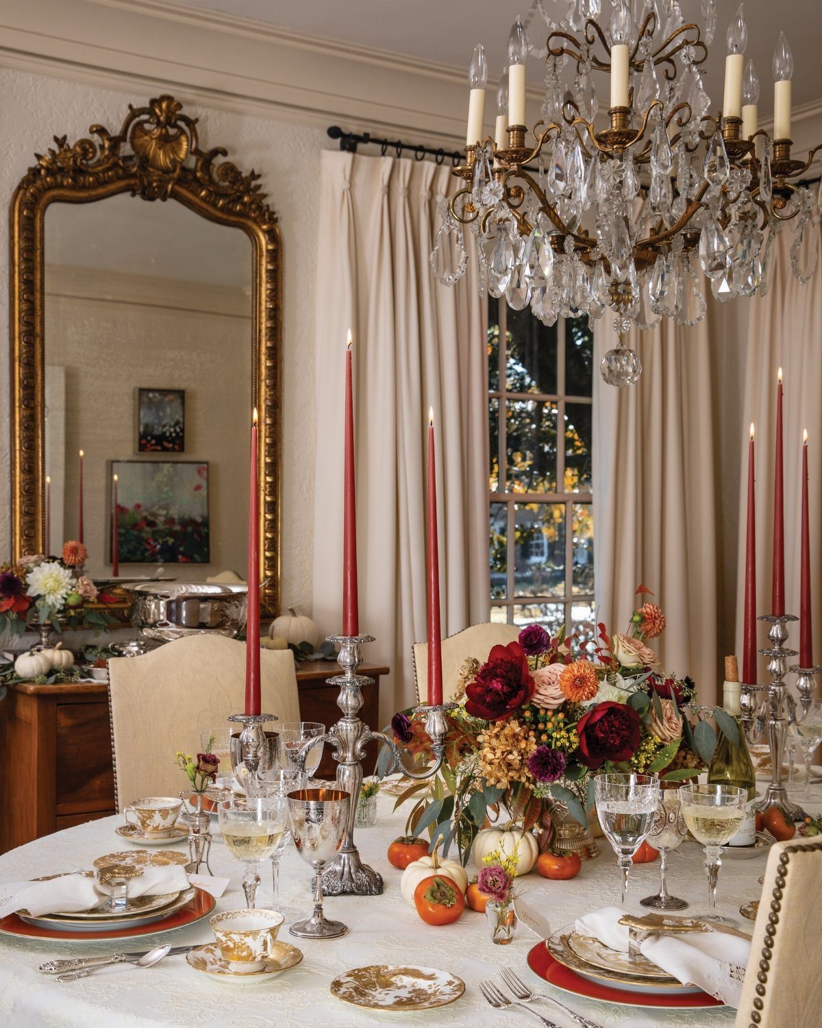 Elegant Thanksgiving table setting with red taper candles, floral centerpiece, and gold-rimmed plates.