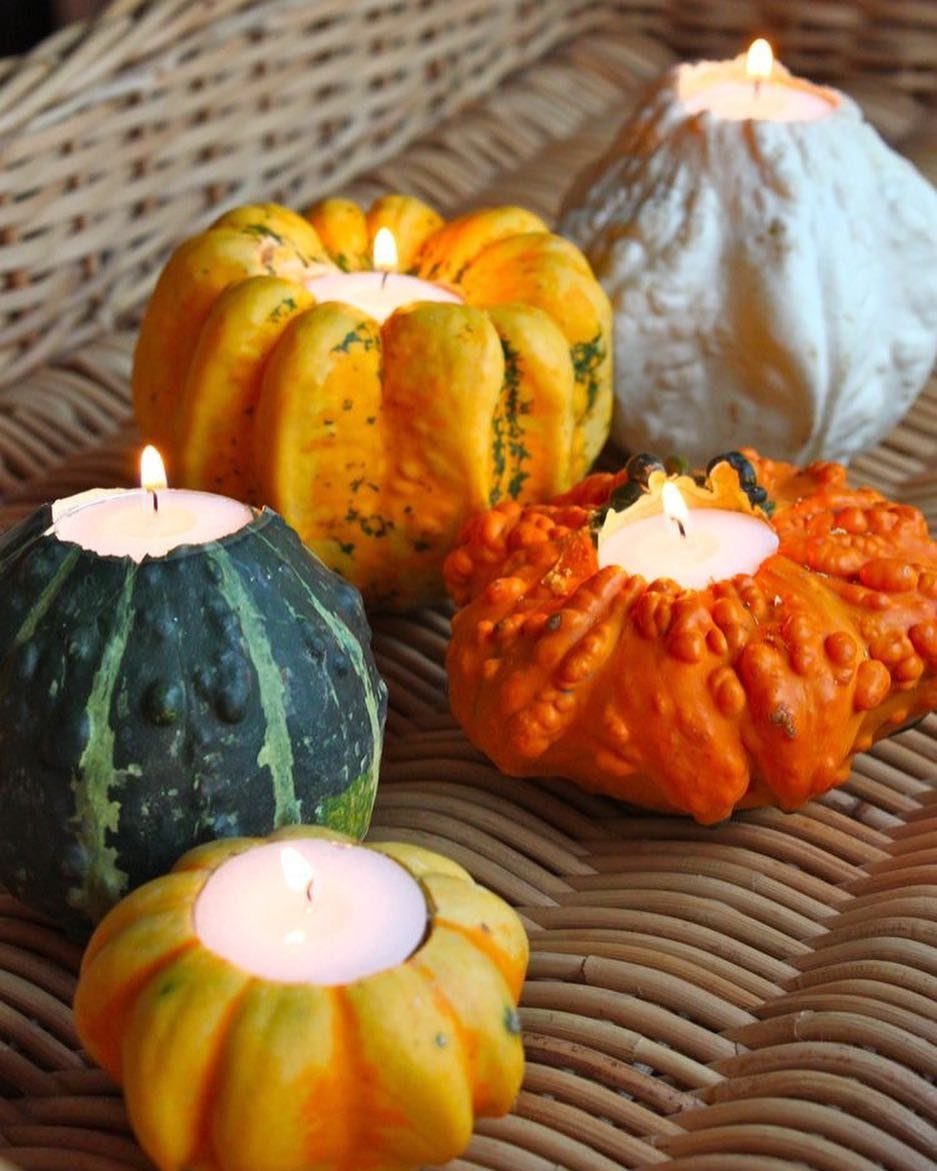 Lit tea light candles nestled inside carved orange, green, and white gourds.