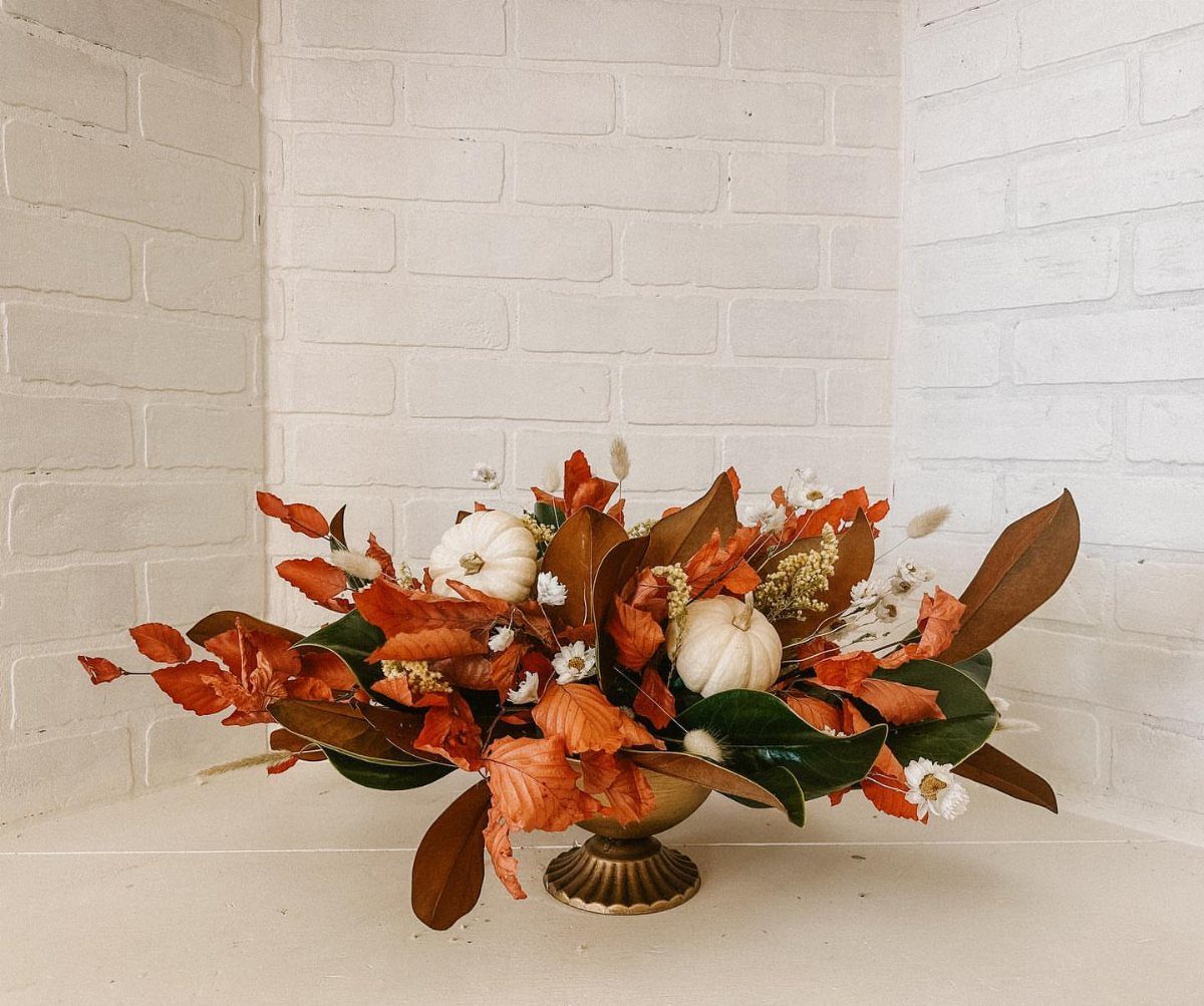 Autumnal floral arrangement with dried orange leaves and white pumpkins in gold bowl