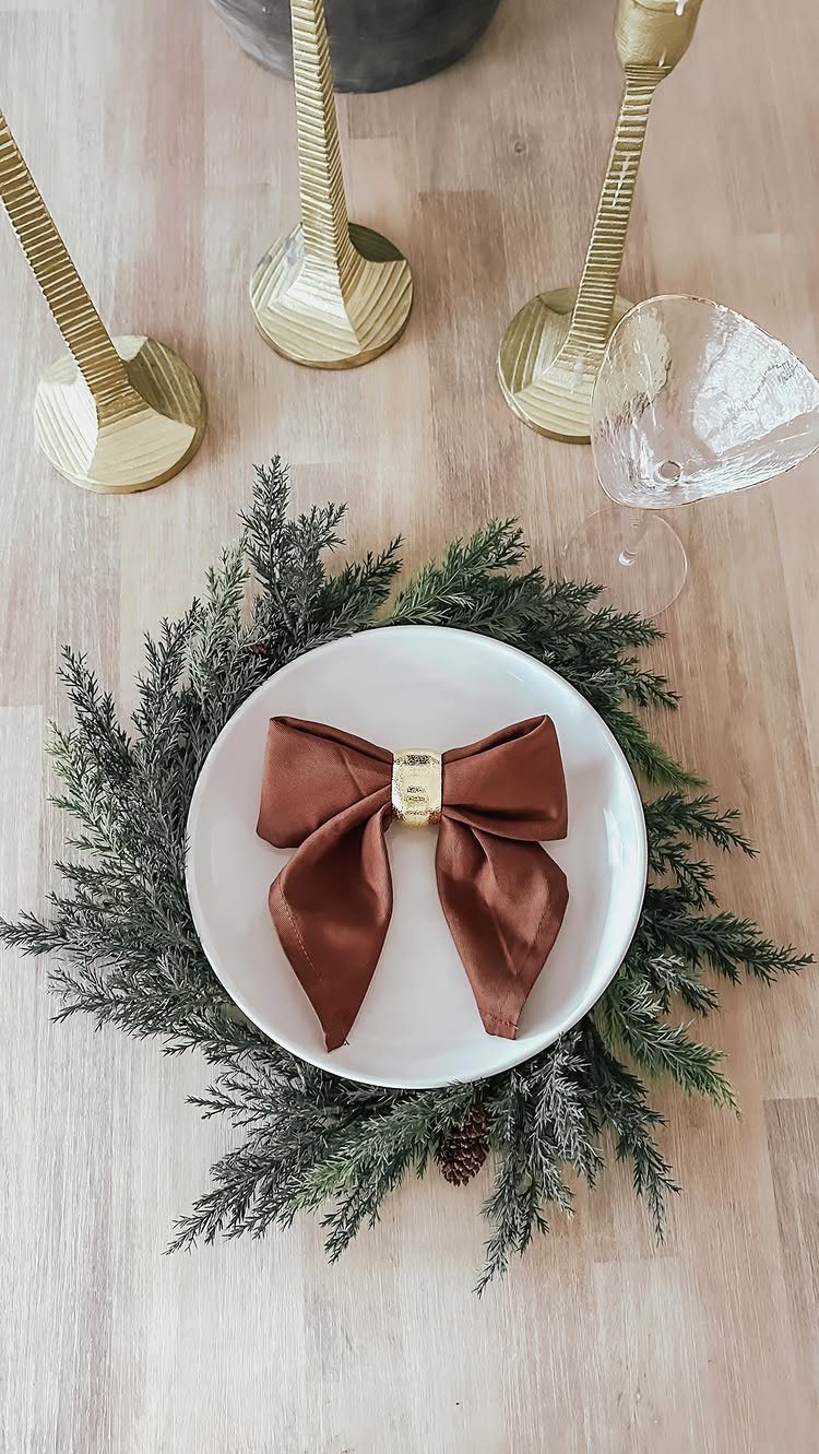 White plate with brown bow napkin on an evergreen wreath table setting
