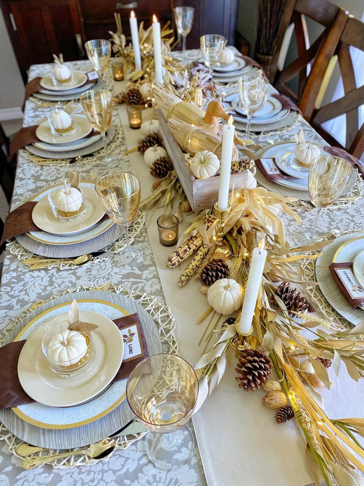 Gold and white table setting with white pumpkins, candles, and dried wheat centerpiece.