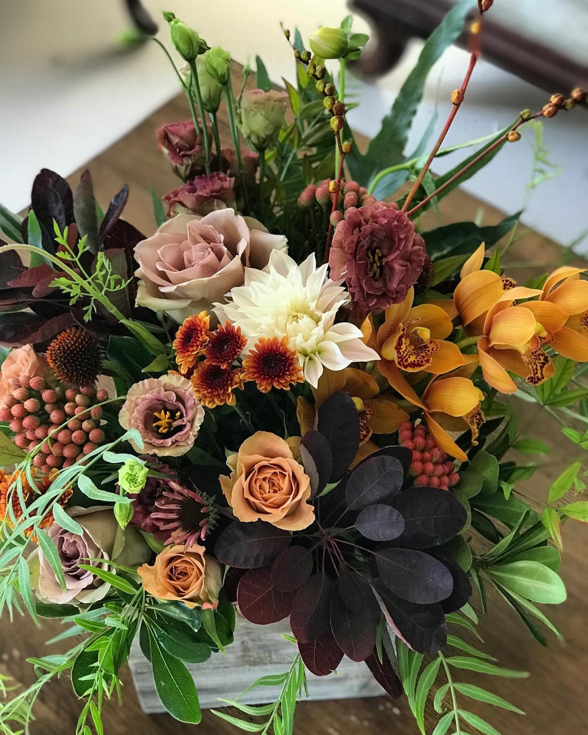 Autumnal floral centerpiece with orange orchids, burgundy roses, and cream dahlias.