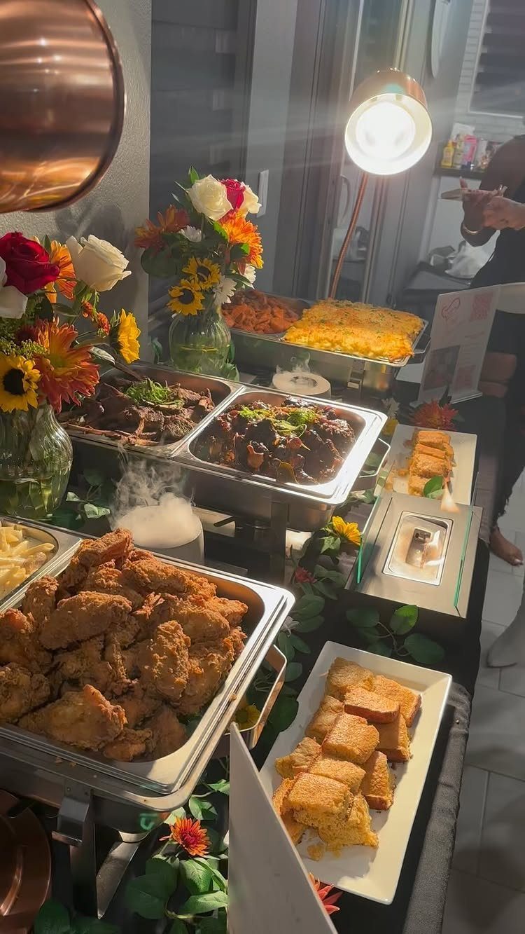 Buffet table with silver chafing dishes of food, cornbread, and colorful floral centerpieces.