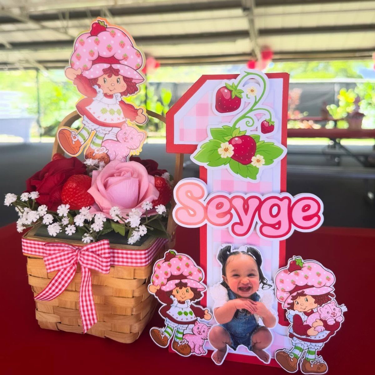Strawberry themed table centerpiece with flowers, a large number one, and baby photo.