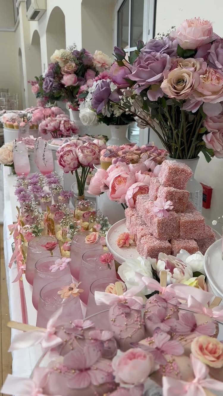 Dessert table with pink drinks, floral arrangements, and pink square treats.