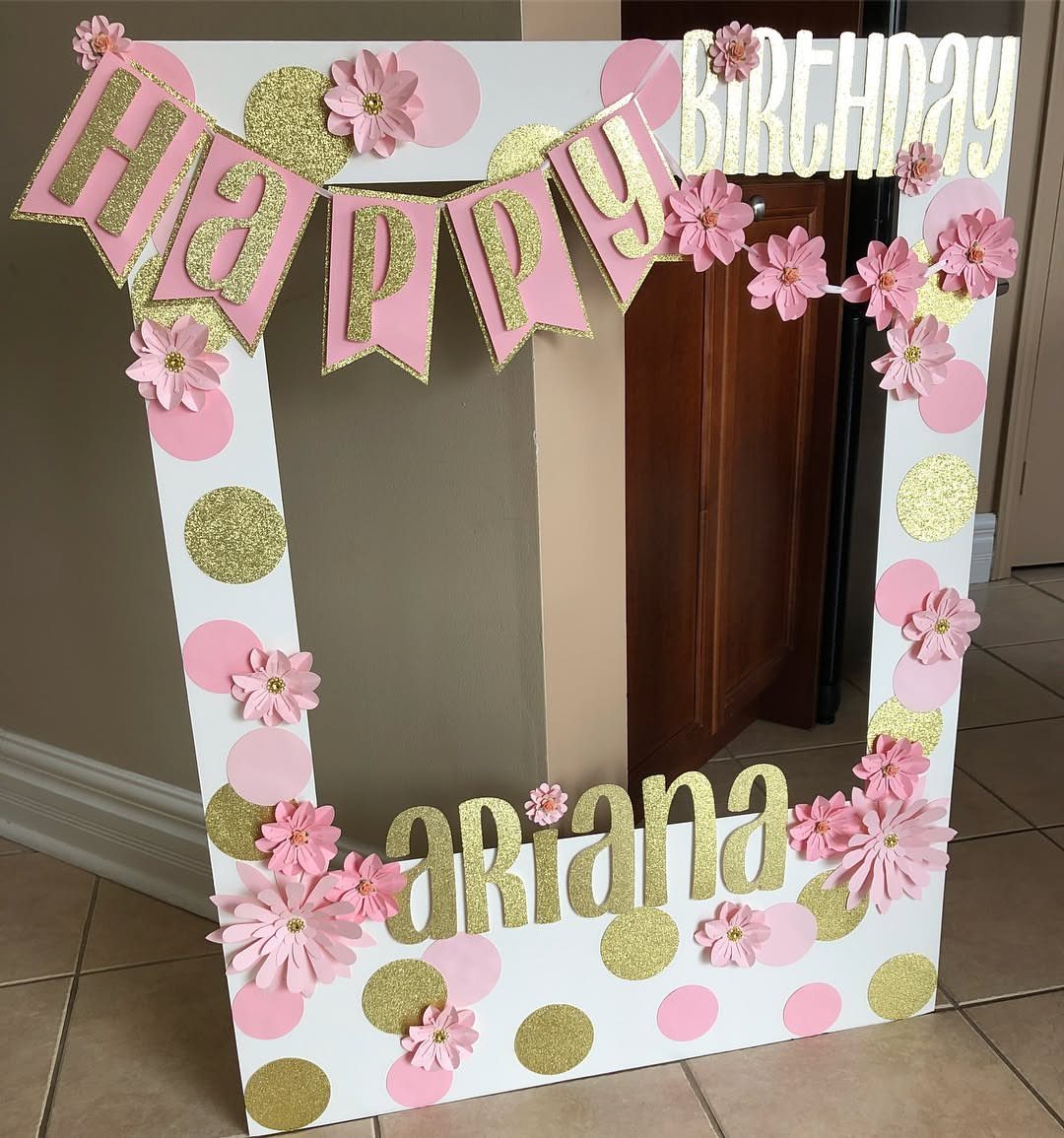 Decorated white photo booth frame with pink flowers and gold glitter accents for Ariana.