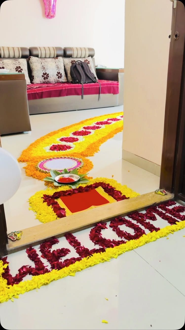 Flower petal rangoli on a white floor spelling welcome in red and yellow.