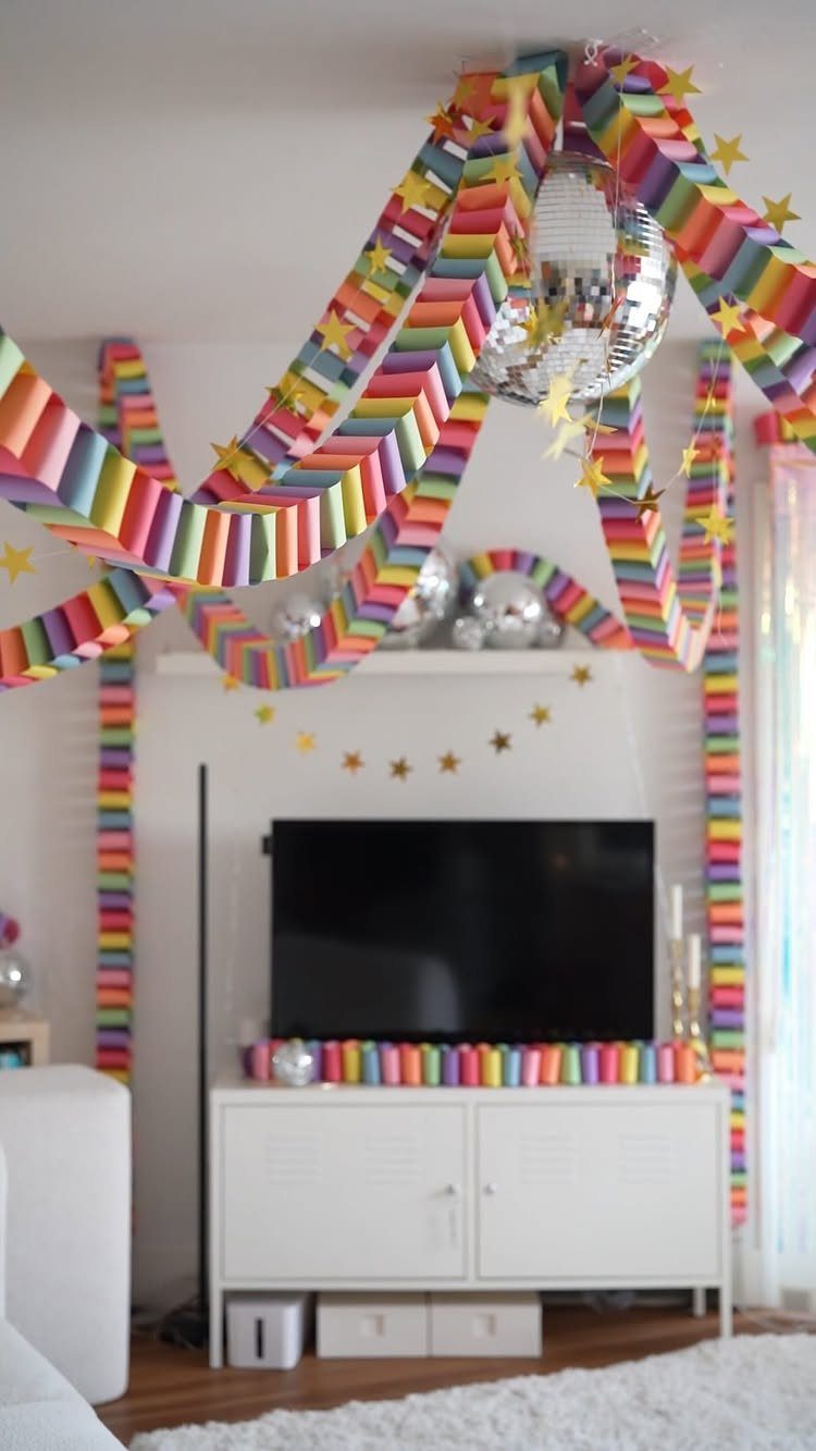 Rainbow paper garlands draped across a room with a disco ball and stars.