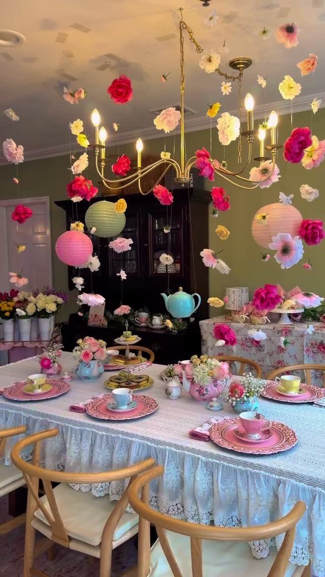 Dining table with pink tea sets and floral decor under hanging paper flowers