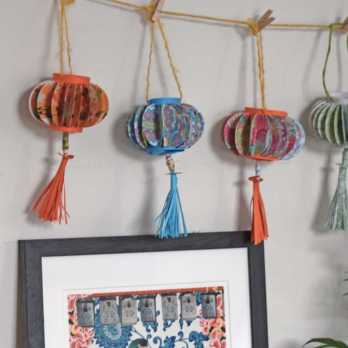 Colorful patterned paper lanterns with tassels hanging from a string above a frame.