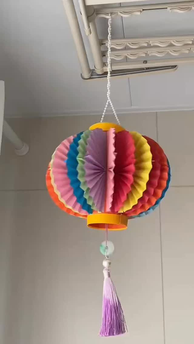 Colorful pleated paper lantern with a purple tassel hanging from a white string.