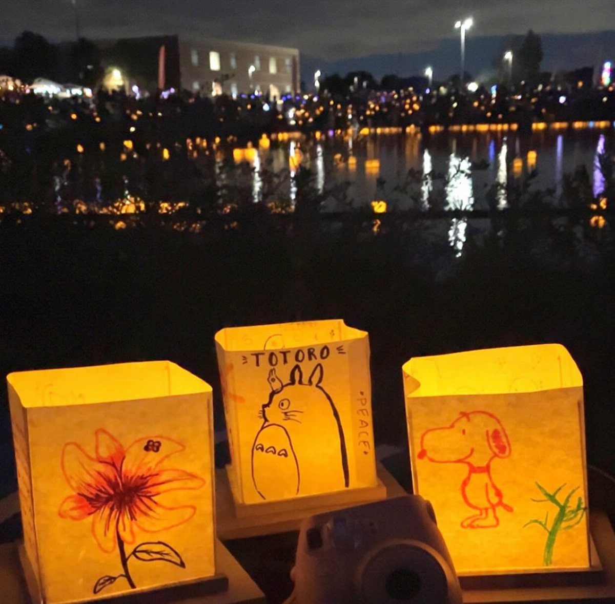 Three glowing yellow paper lanterns with drawings of Totoro and Snoopy at night
