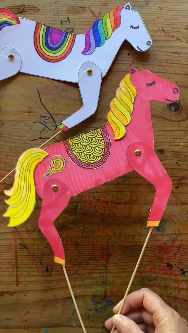 Colorful paper horse puppets with movable legs held by wooden skewers on wood.