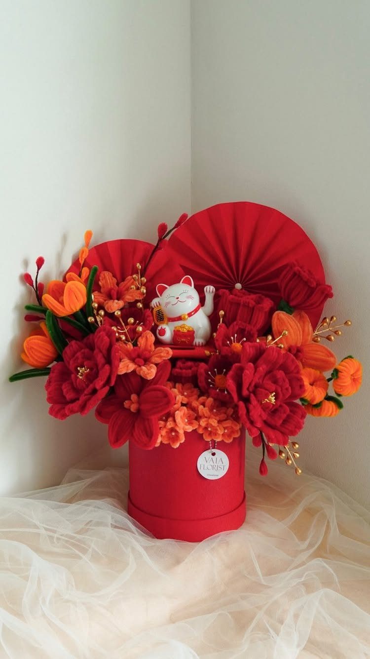 Red gift box with orange and red flowers, folding fans, and lucky cat figurine.
