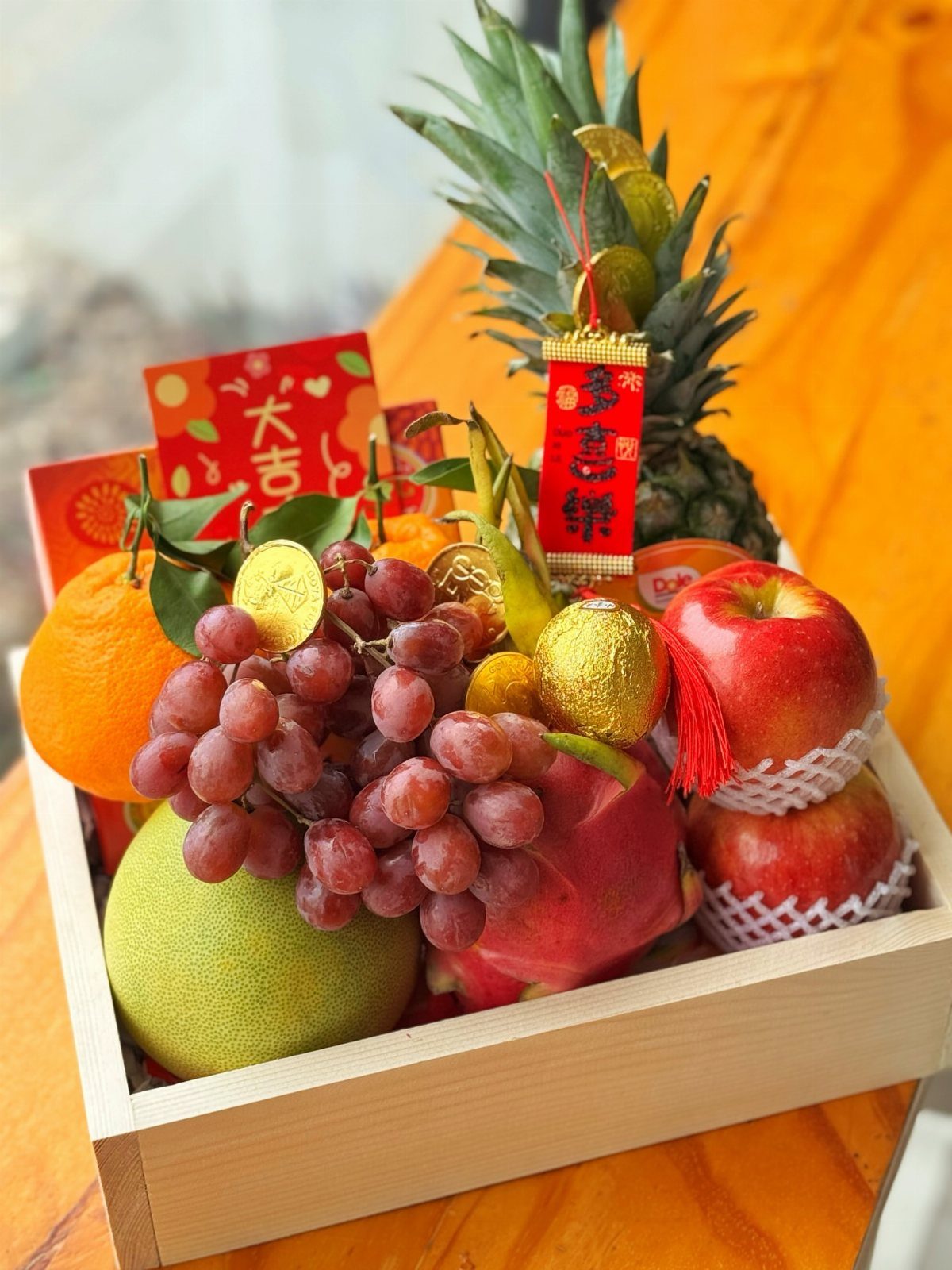 Wooden crate of festive fruits and red Chinese New Year cards with a pineapple.