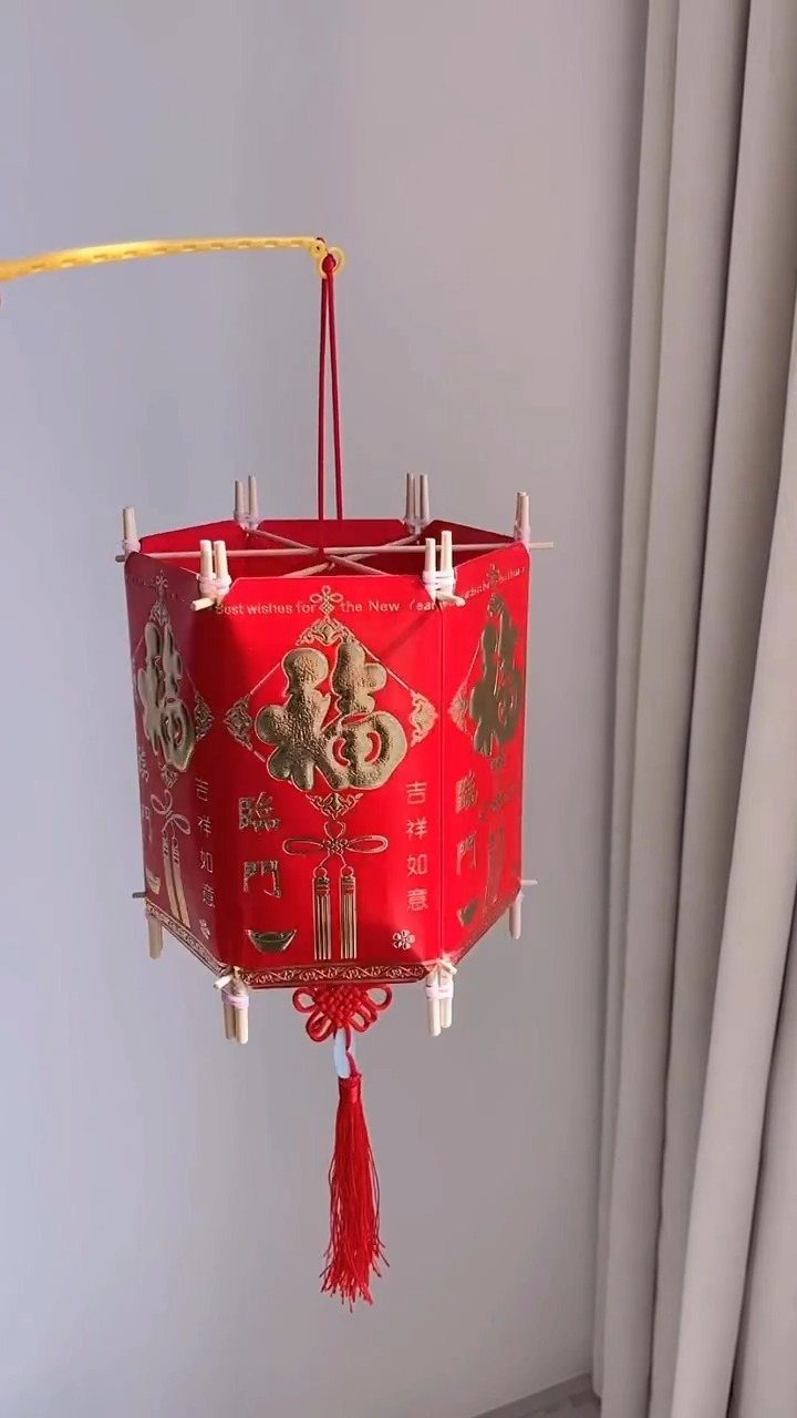 Red Chinese lantern with gold patterns and a tassel hanging against a wall