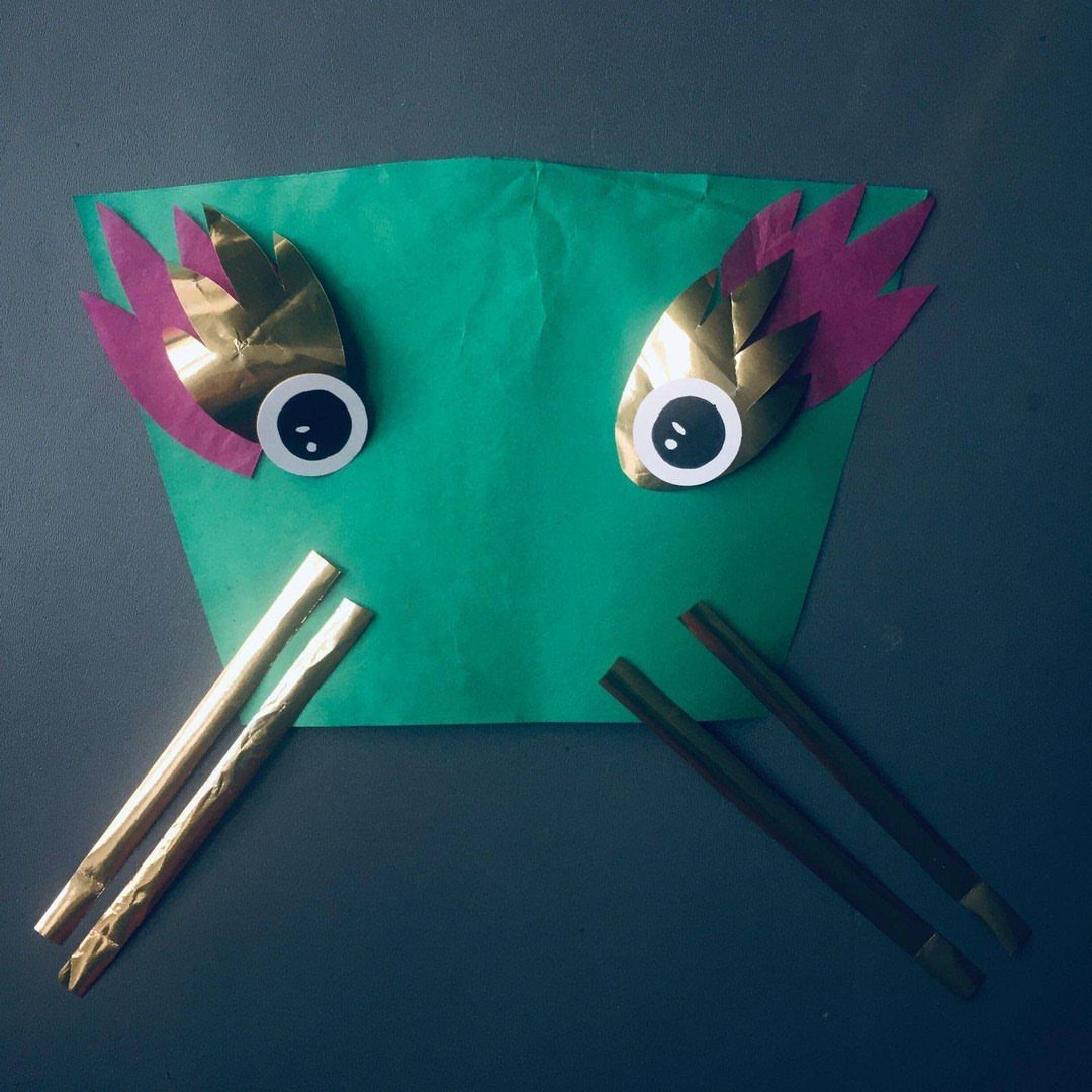 Handmade green paper dragon face with gold accents and gold stick whiskers.