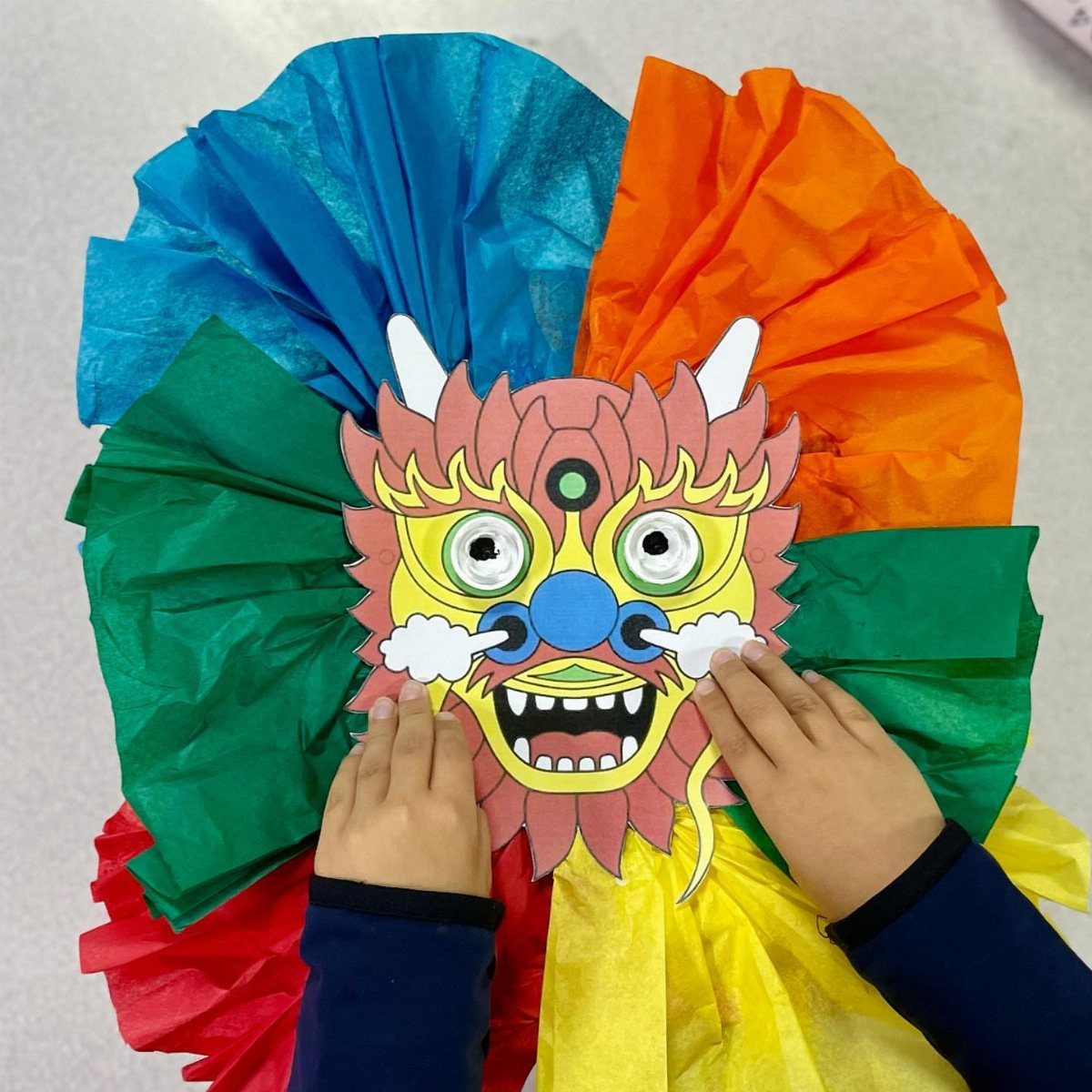 Child holding a colorful paper dragon mask over bright pleated tissue paper