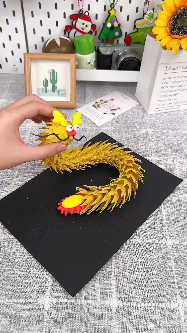 Yellow paper strip dragon craft with googly eyes on a black background.